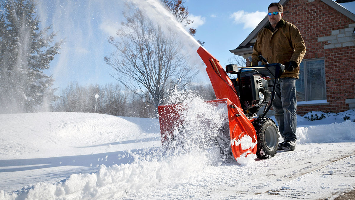 Уборка снега ручным снегоуборщиком во дворе загородного дома