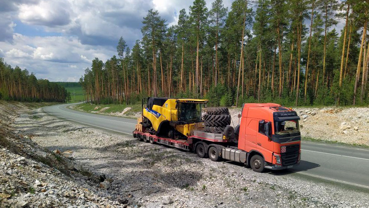 Грузовик с тралом перевозит строительную технику по лесной дороге